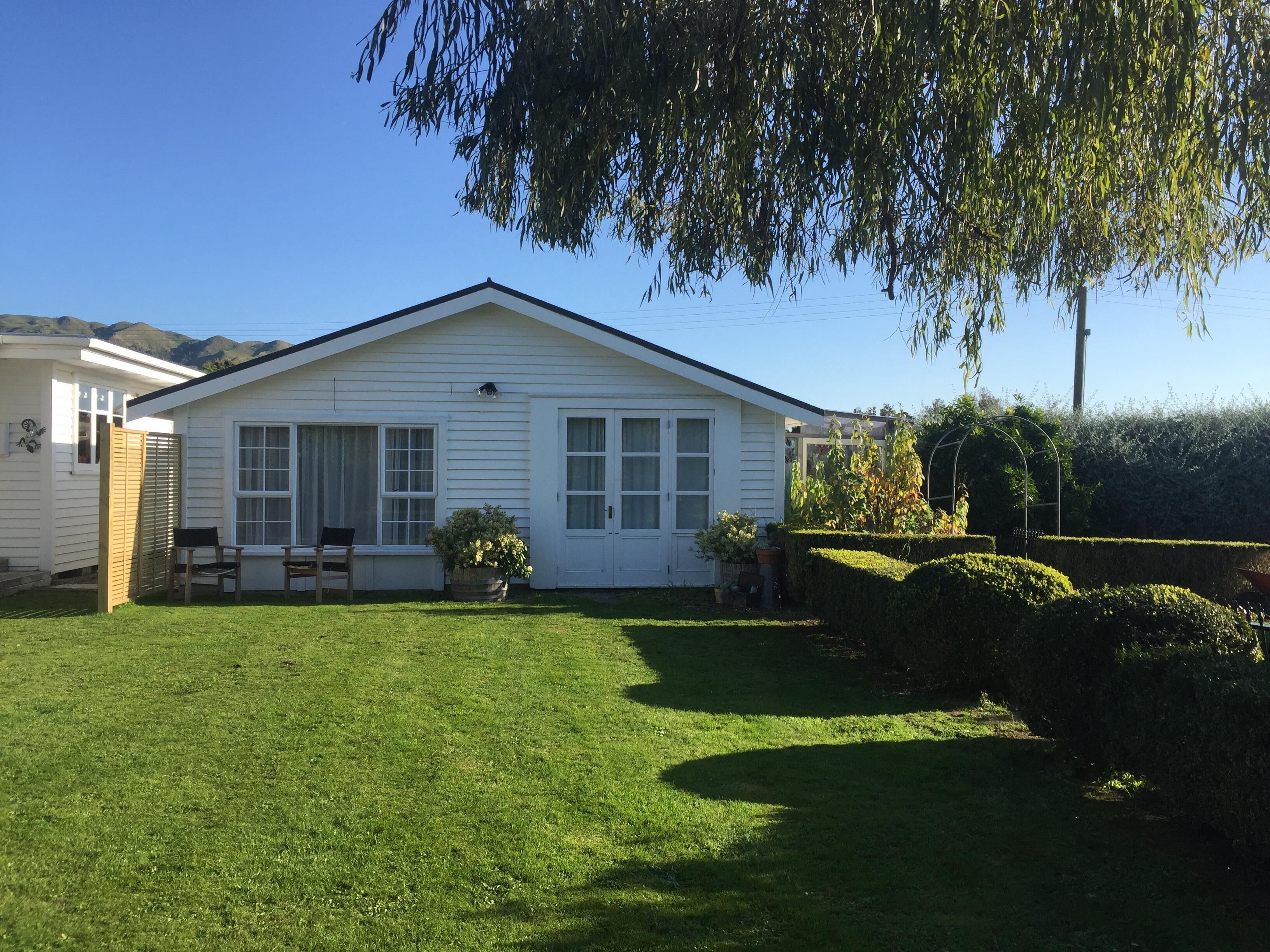 A single-story white house with a front porch, a small garden, and a clear blue sky.
