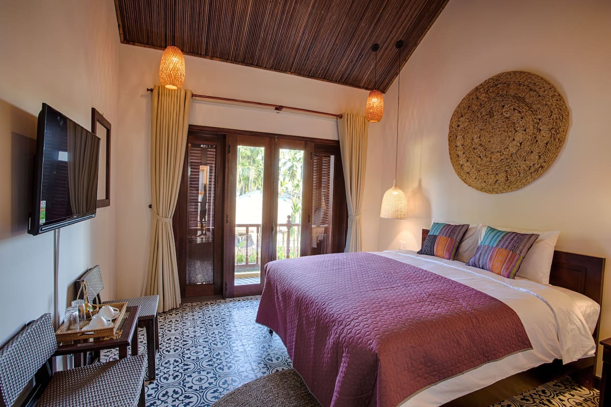 A hotel room with a bed, a TV, a desk with a chair, and a view of the outdoors.