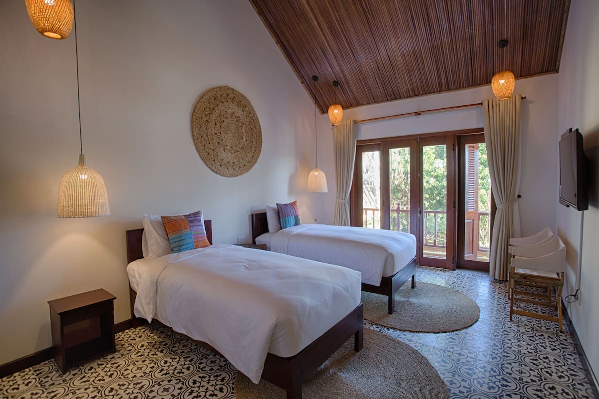 A room with two beds, a wooden ceiling, woven wall hangings, and a patterned floor.
