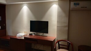 Una habitación con televisión de pantalla plana en una pared texturizada, un escritorio de madera con una silla y un pequeño calefactor sobre el escritorio.