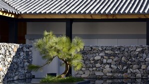 A traditional Japanese-style building with a tiled roof, a stone wall, and a bonsai tree in a reflective water feature. - The Rock Hotel (Lijiang)