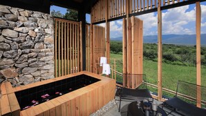 A wooden spa area with a stone wall, a hot tub, and a view of the landscape. - The Rock Hotel (Lijiang)
