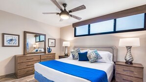 Ein Schlafzimmer mit einem großen Bett, einem Deckenventilator, einem Schminktisch, Nachttischlampen und Bildern an den Wänden.