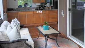 Un porche cubierto con un sofá, una mesita y una zona de cocina con armarios de madera y dispensador de agua.