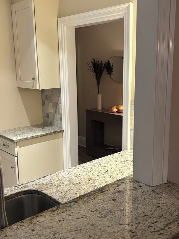 A kitchen with a granite countertop, a stainless steel sink, and a white cabinet.