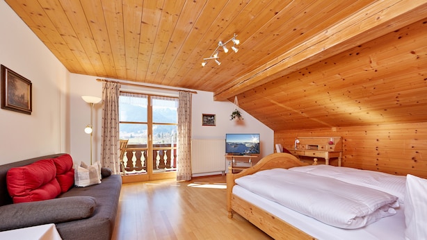 A cozy room with a wooden ceiling, a bed, a sofa, a TV, and a view of the outdoors. - Bauernhof Buchwieser (Unterammergau)
