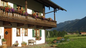 A traditional chalet with a balcony adorned with colorful flowers, a wooden door, and a bench outside. - Bauernhof Buchwieser (Unterammergau)