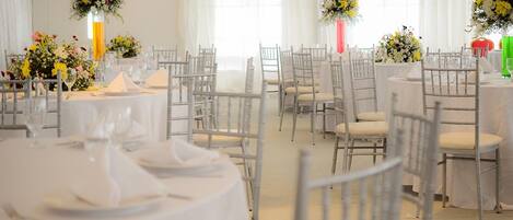 A banquet hall with round tables, white chairs, and floral centerpieces.