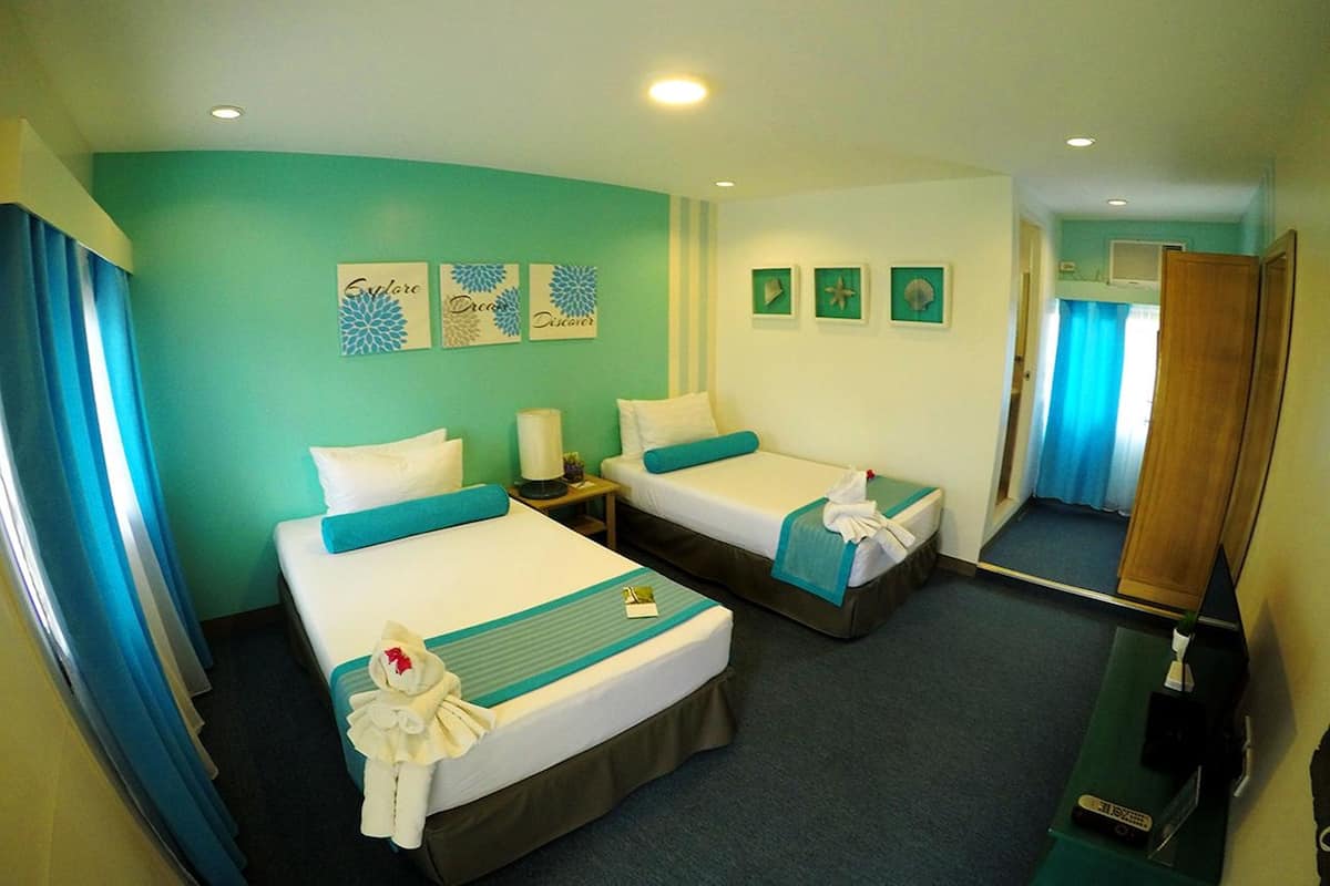 Quarto de hotel com duas camas, paredes verde-água e um espelho.