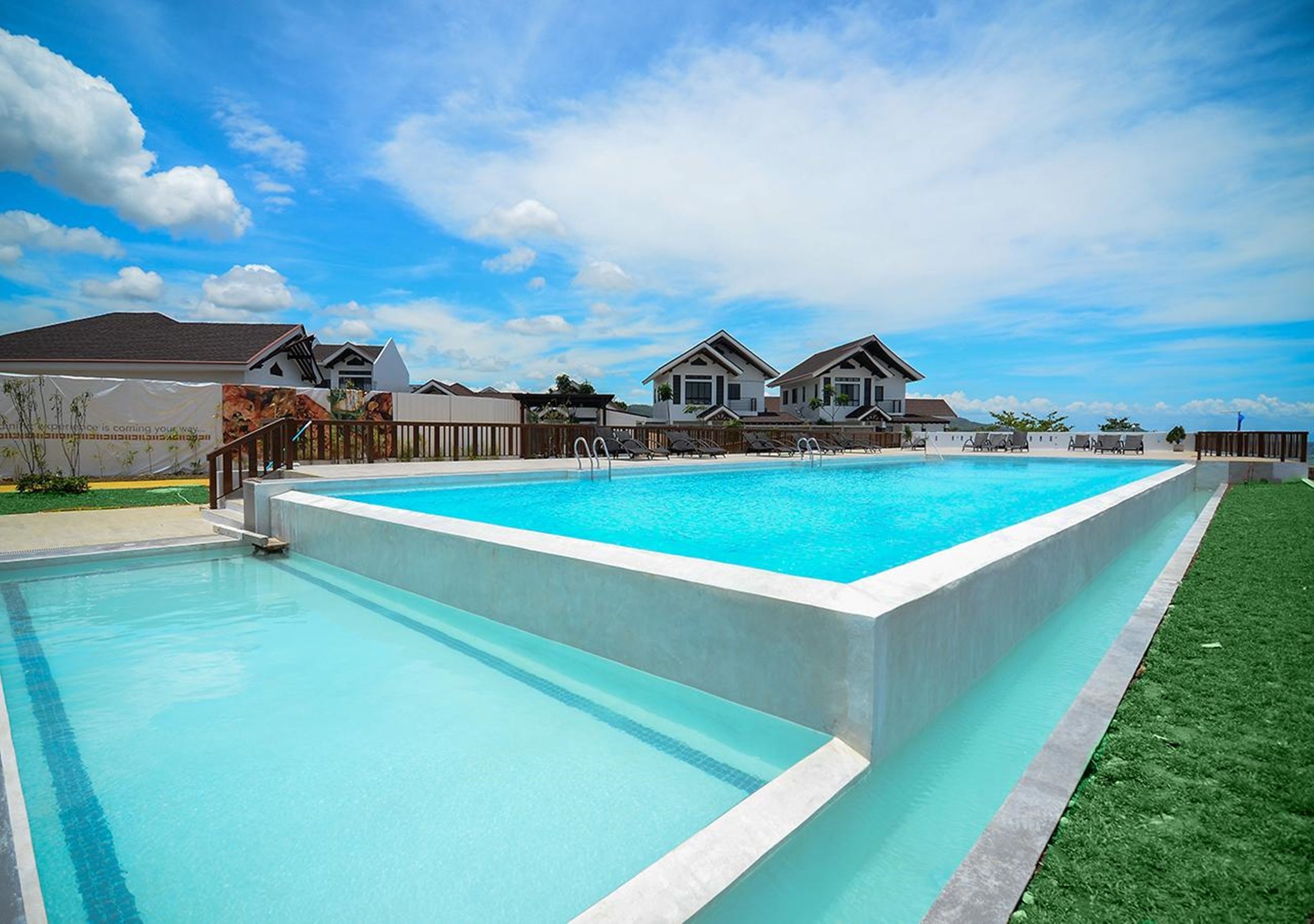 A rectangular swimming pool with a wooden deck and a grassy area on one side.