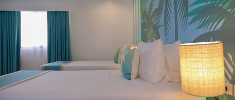 Habitación de hotel con dos camas, cortinas color turquesa, un mural de palmeras y una lámpara encendida.