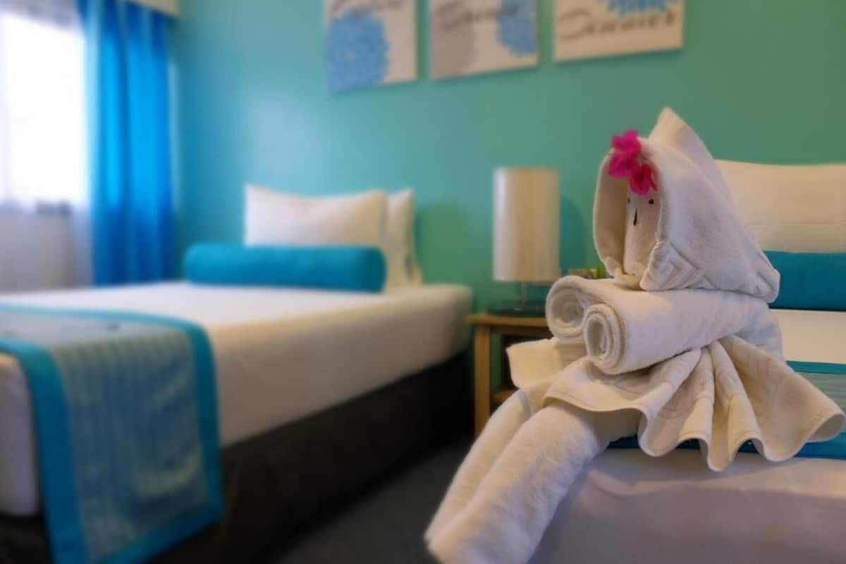 Quarto de hotel com duas camas, uma mesa de cabeceira com abajur e uma parede com obras de arte.