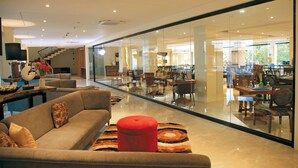 Amplia sala de estar con un sofá moderno, un reposapiés rojo y un panel de vidrio que separa la sala del comedor.