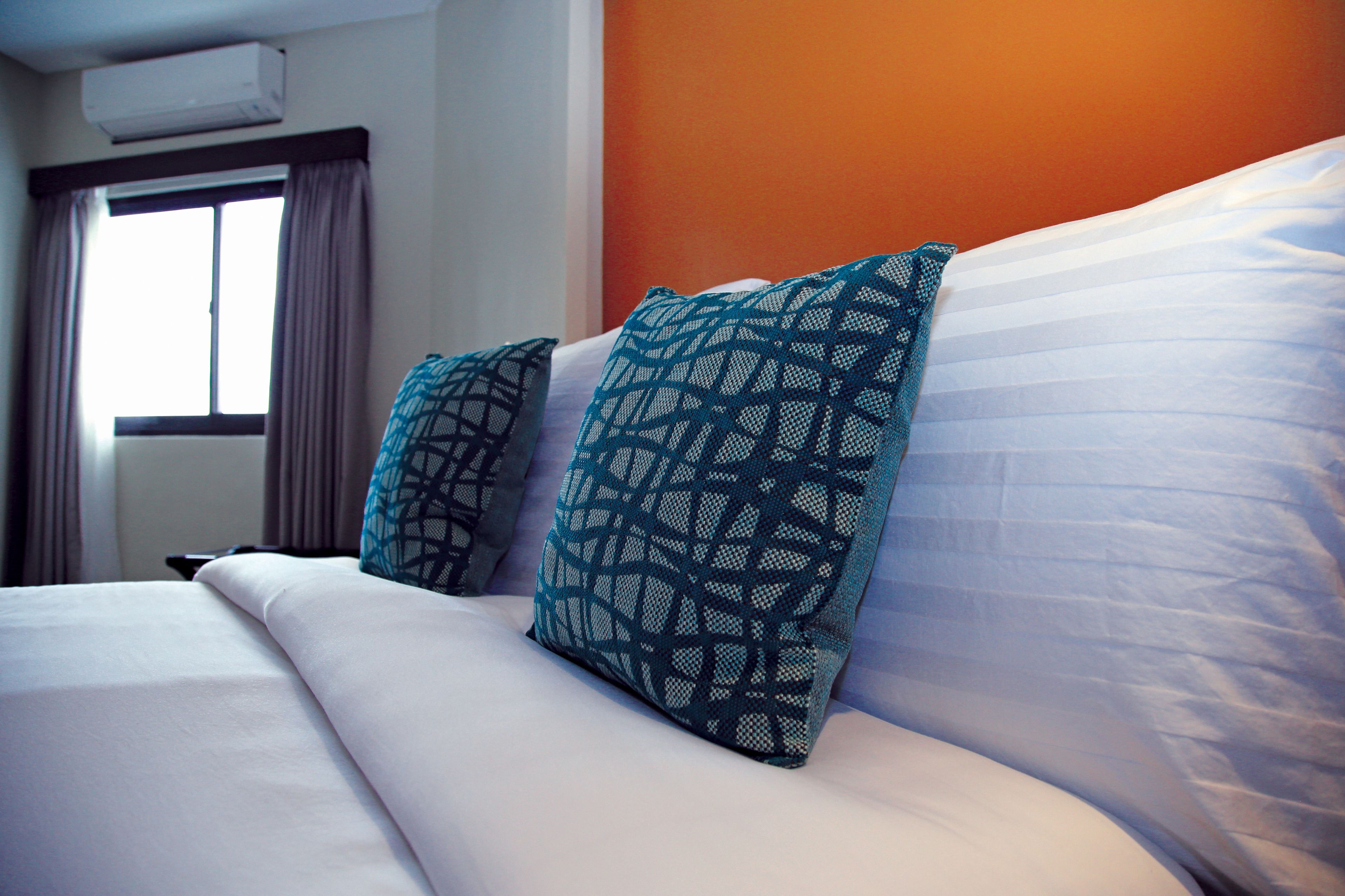 A neatly made bed with white linens and two patterned pillows.