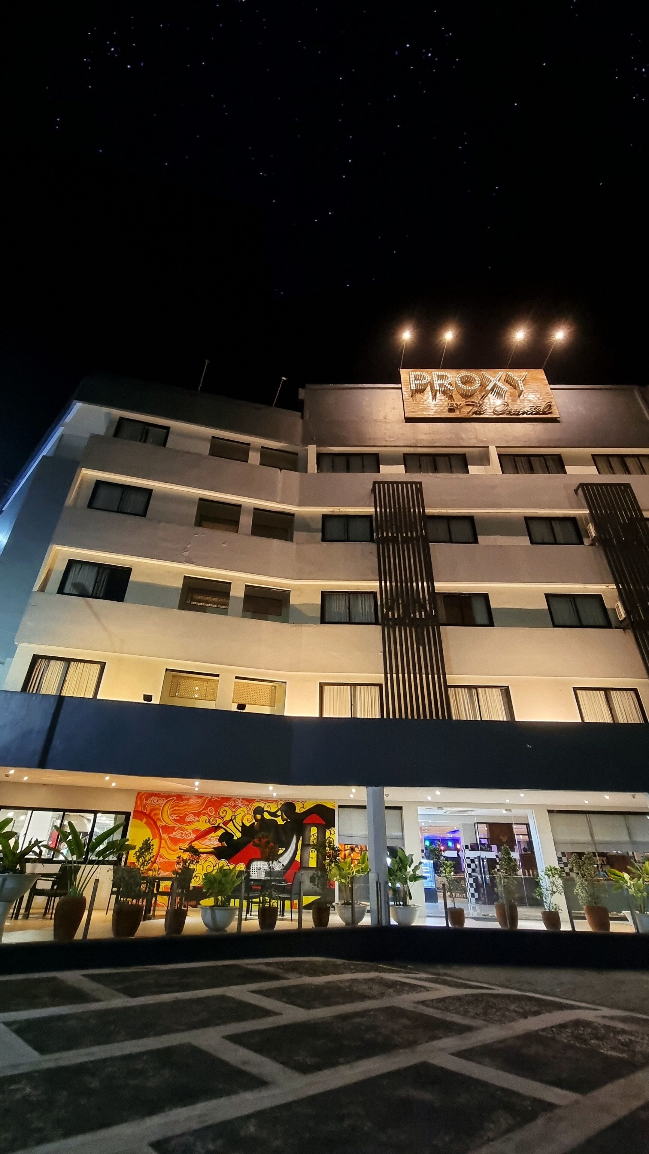 A multi-story hotel with a modern facade, illuminated signage, and a vibrant mural at the entrance.