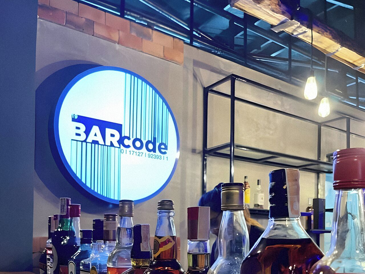 En bardisk med en stor, rund skylt som visar texten ”BARCODE” och olika sorters spritflaskor uppradade på disken.