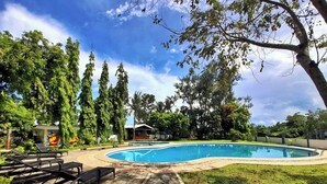 Una piscina con sillones de descanso, rodeada de árboles y un edificio con un mural.