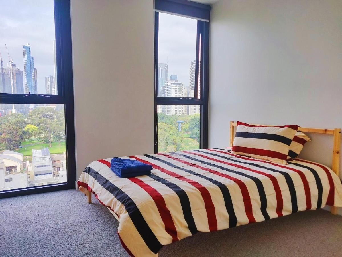 A bedroom with a large window, a bed with striped bedding, and a view of buildings and greenery outside.