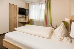 A hotel room with a bed, a television on a stand, a small table, and a chair. - Landhotel Wolf-Mertes (Sessenbach)