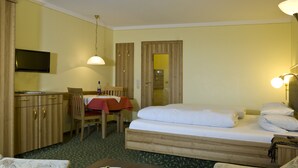 A hotel room with a bed, a desk, a chair, a television, and a dining table with a red tablecloth. - Appartementhof Aichmühle (Bad Fuessing)