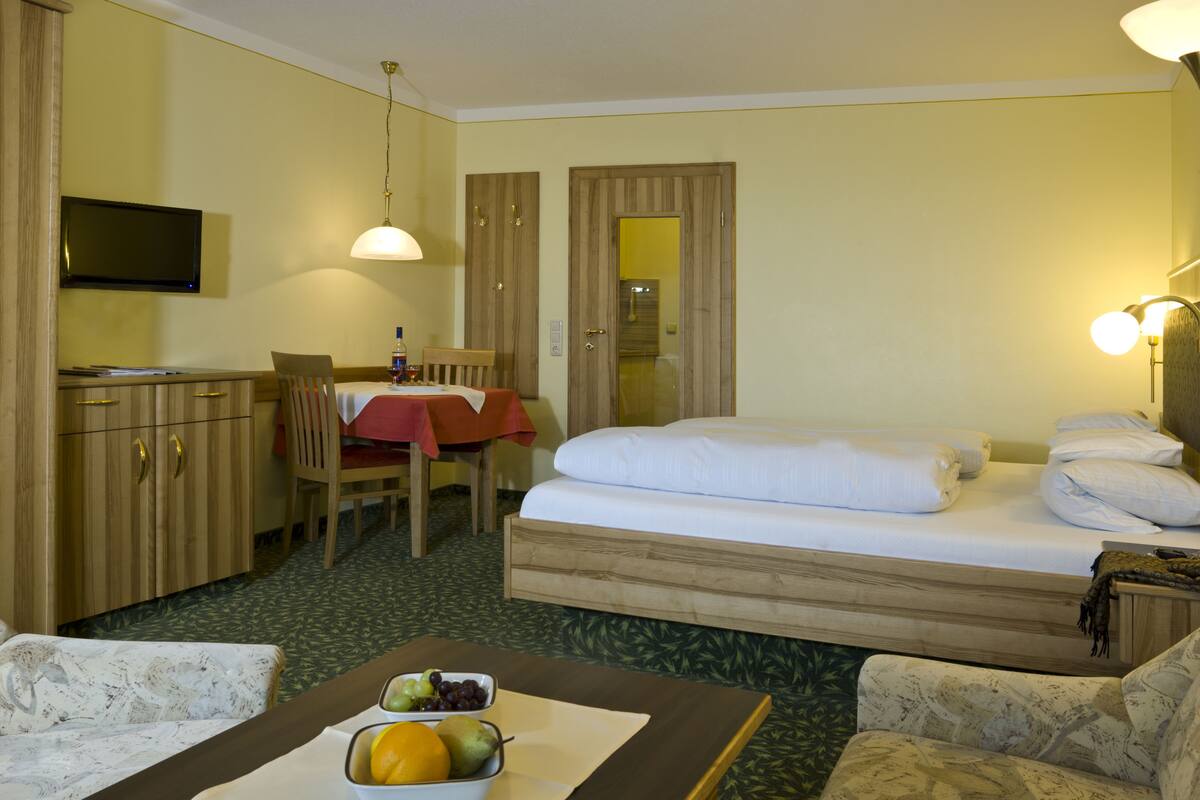 Une chambre d’hôtel comprenant un lit, un bureau, une chaise, un téléviseur et une table à manger recouverte d’une nappe rouge.