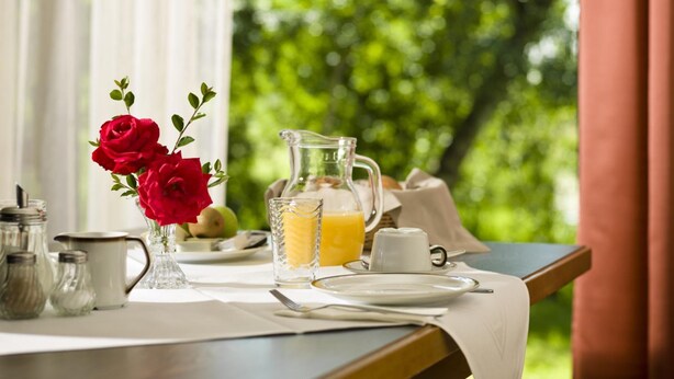 A breakfast setting with a pitcher of orange juice, a vase of red roses, and a table with plates and utensils. - Appartementhof Aichmühle (Bad Fuessing)