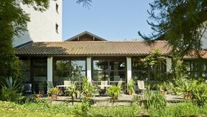 A covered outdoor seating area with tables and chairs, surrounded by potted plants and greenery. - Appartementhof Aichmühle (Bad Fuessing)