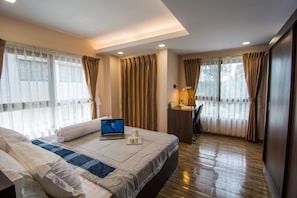 A hotel room with a bed, a desk with a laptop, a lamp, and curtains. - Rose Villa Residence (Yangon)