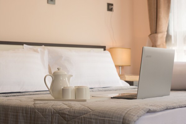 A neatly made bed with a laptop, a teapot, and cups on a tray, suggesting a hotel room setting.