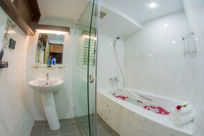A modern bathroom with a glass-enclosed shower, a pedestal sink, and a freestanding bathtub with rose petals.