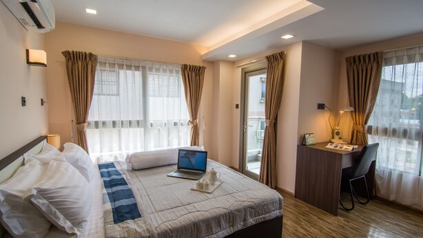 Una habitación de hotel con cama, escritorio, computadora portátil y ventana con cortinas.