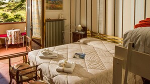 Habitación de hotel con cama, una silla, una mesa con cojín rojo y vista a follaje exterior.