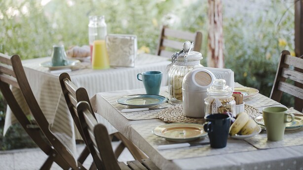 Una mesa lista para el desayuno, con platos, tazas y un tarro de azúcar.