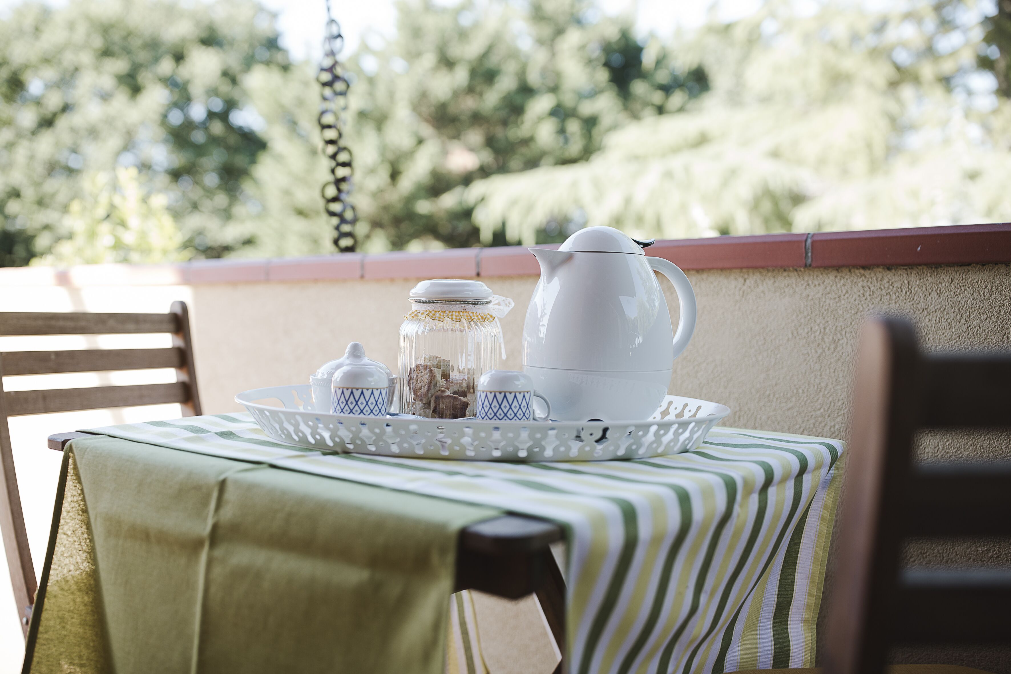 Een tafel met een dienblad waarop een theepot, suikerpot en een glazen pot staan, bedekt met een groen gestreepte tafelkleed.