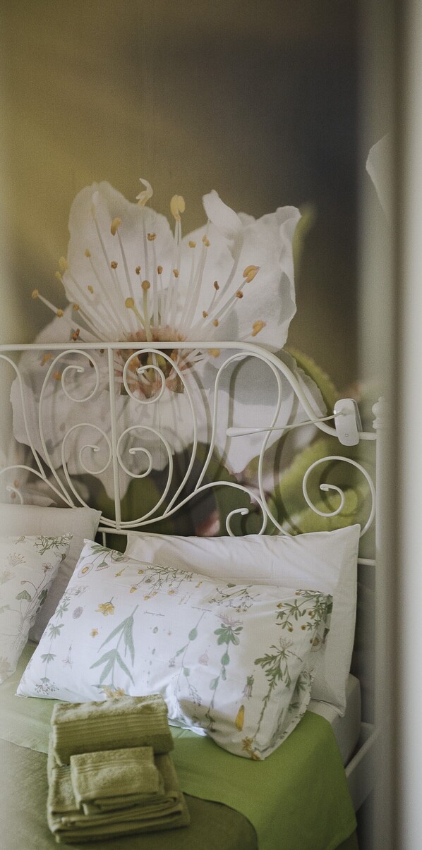A bed with a white metal headboard, a floral pillow, and a green bedspread.