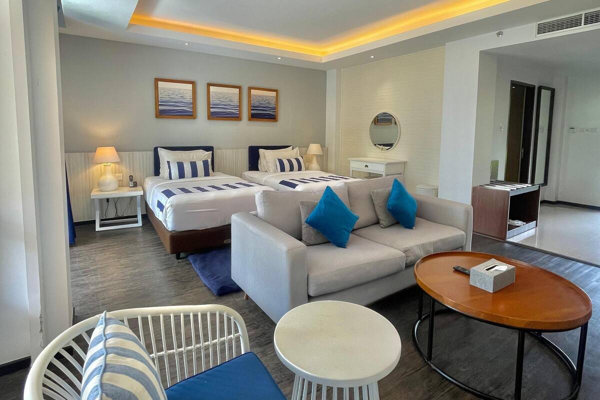 Une chambre d’hôtel moderne équipée d’un canapé, d’un fauteuil, d’une table basse et d’un lit avec des coussins assortis.