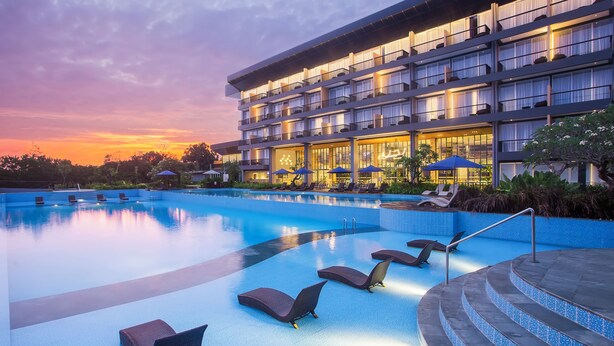 A modern hotel with a swimming pool, sun loungers, and a well-lit building facade.