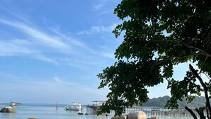 A beach with clear water, large rocks, and a pier in the background.