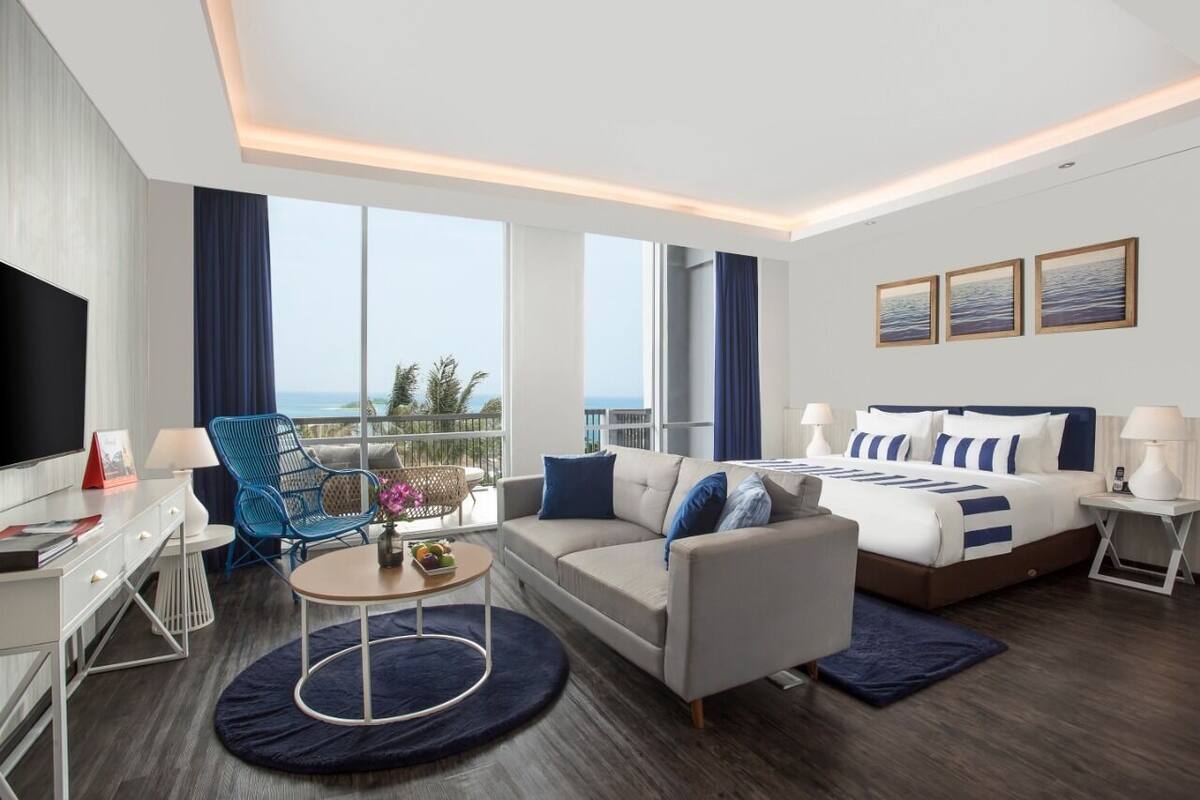 Une chambre d’hôtel moderne dotée d’un grand lit, d’un canapé, d’une télévision et d’un balcon offrant une vue sur l’océan.