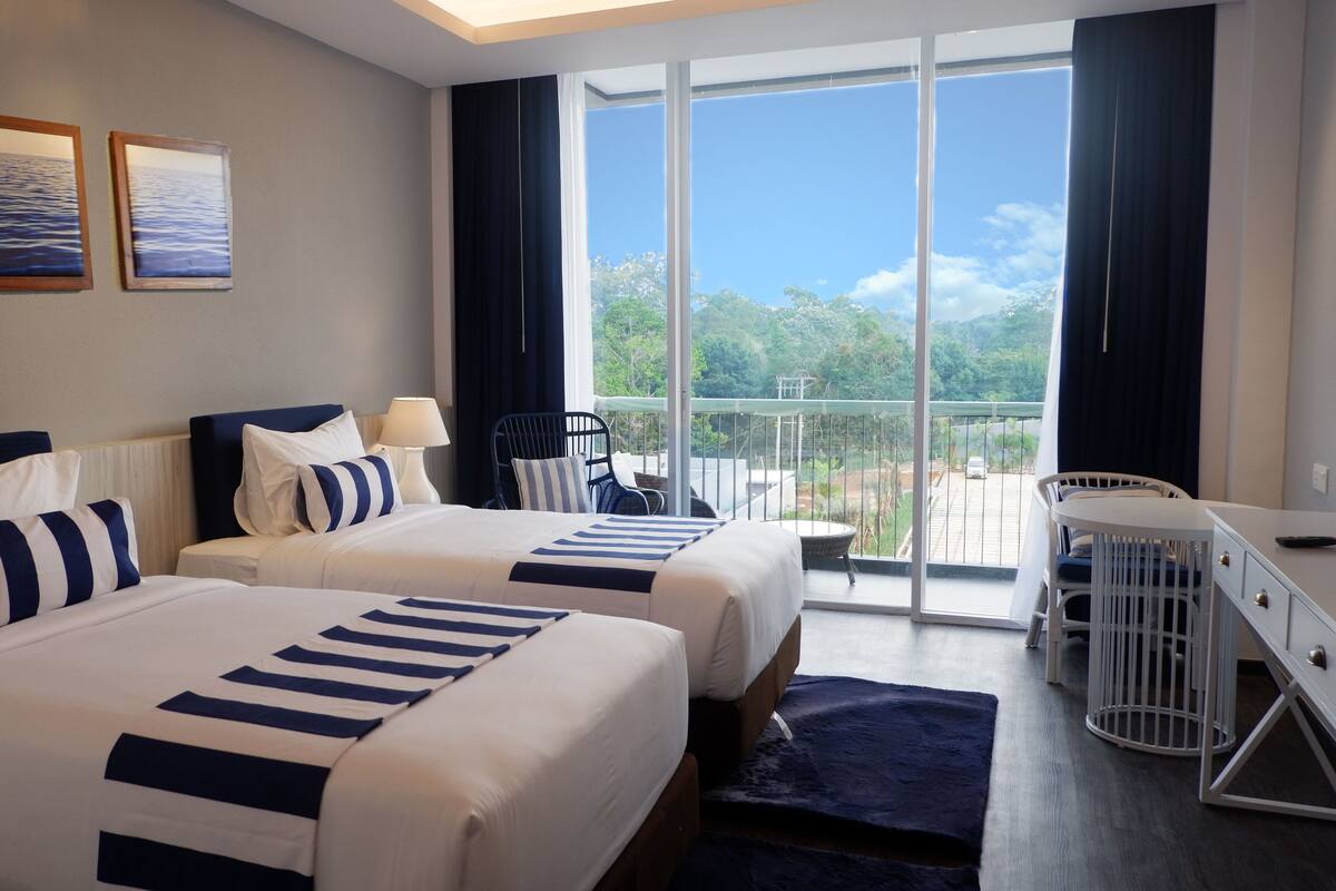 Une chambre d’hôtel avec deux lits, un bureau, une chaise et un balcon avec vue.