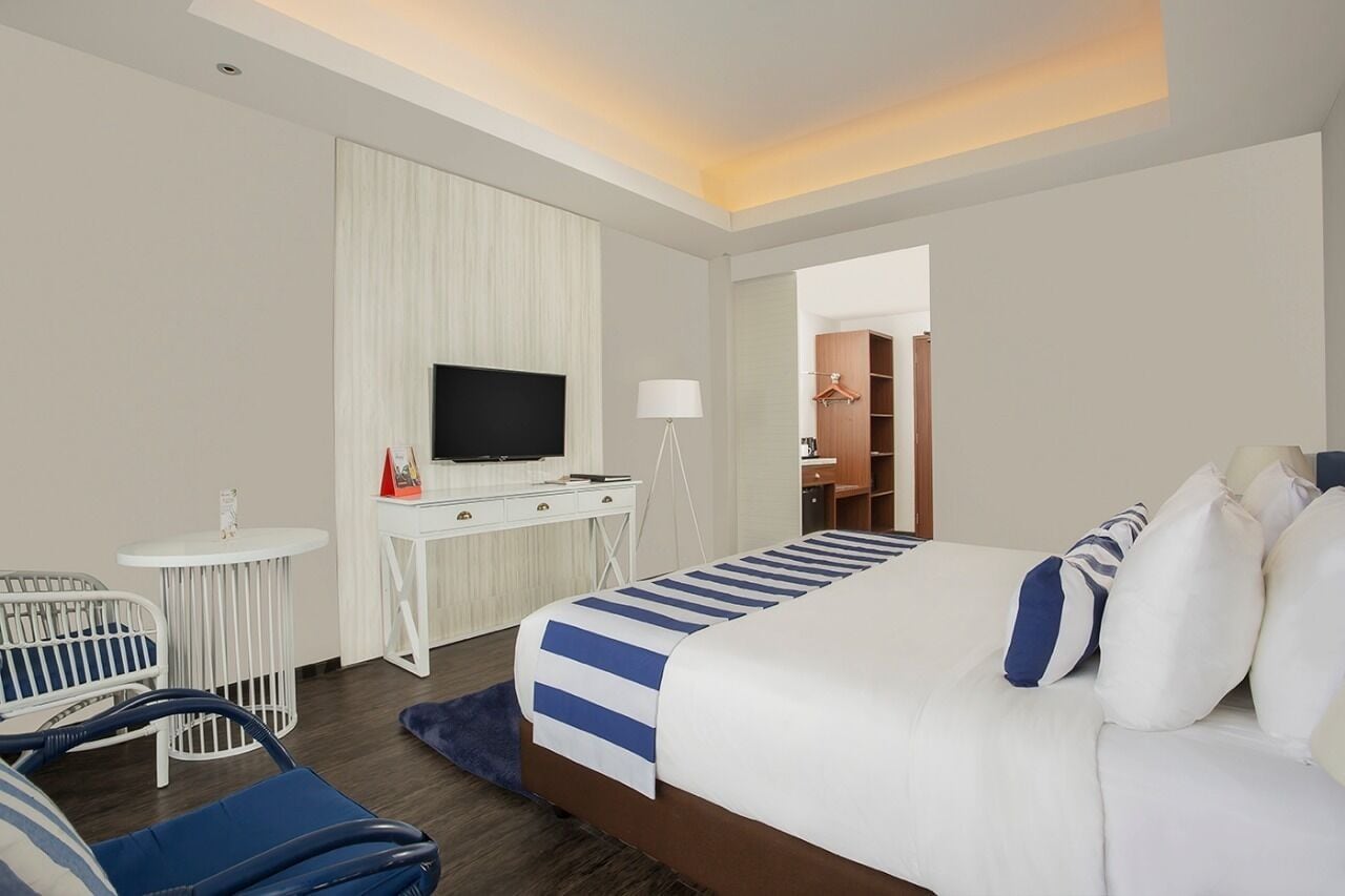 A hotel room with a bed, a desk with a TV, a chair, and a wardrobe.