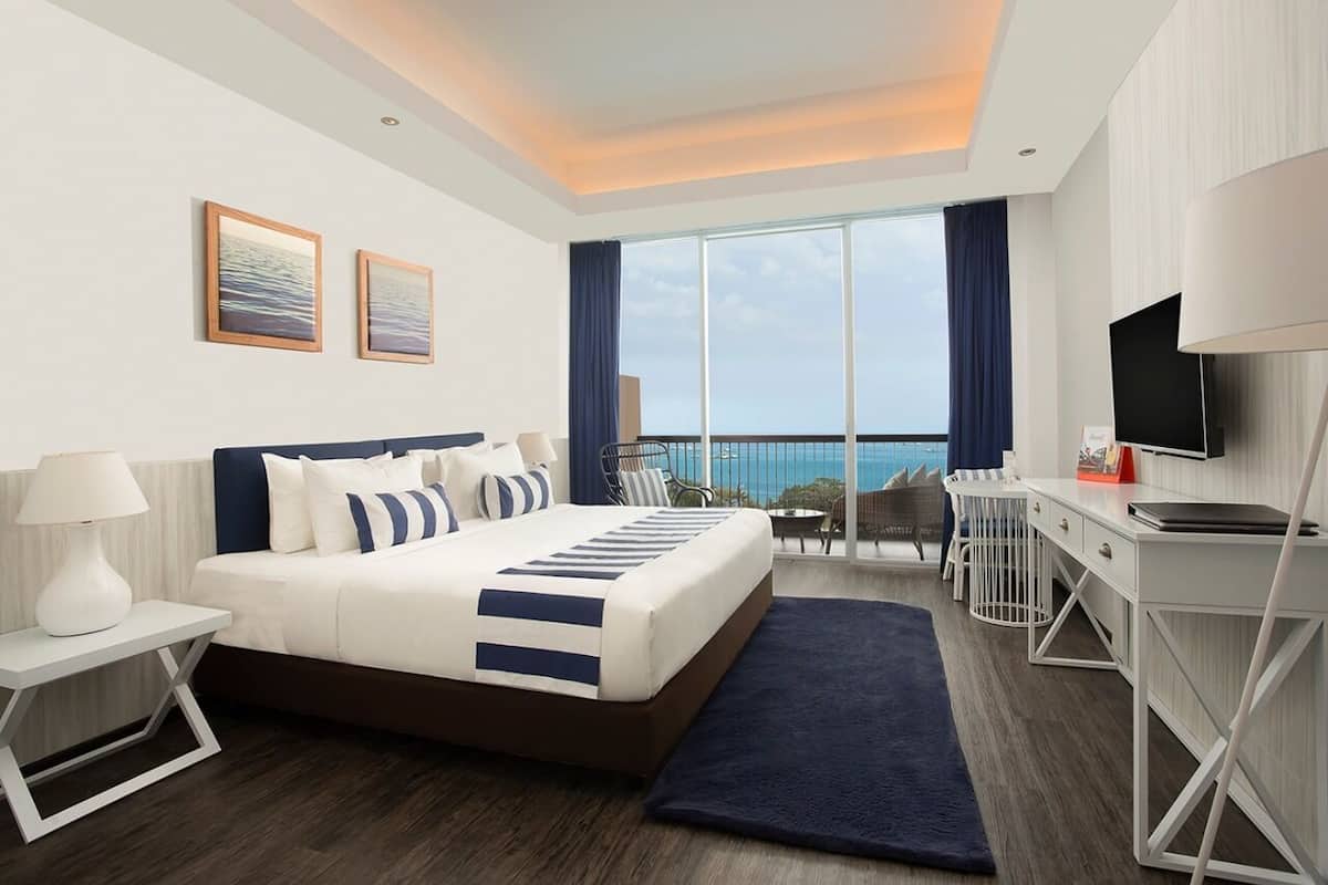 Une chambre d’hôtel moderne dotée d’un grand lit, d’un bureau, d’une télévision et d’un balcon offrant une vue sur l’océan.