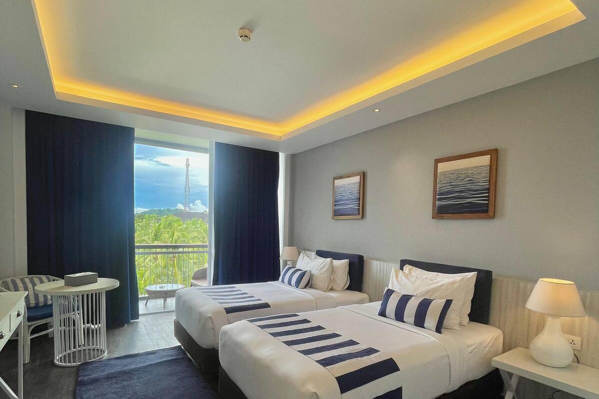 Une chambre d’hôtel moderne avec deux lits, un balcon, un bureau et une vue sur l’extérieur.