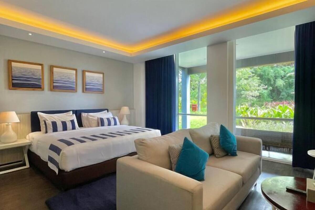Une chambre d’hôtel avec un lit, un canapé, une table de chevet et une fenêtre donnant sur un paysage verdoyant.