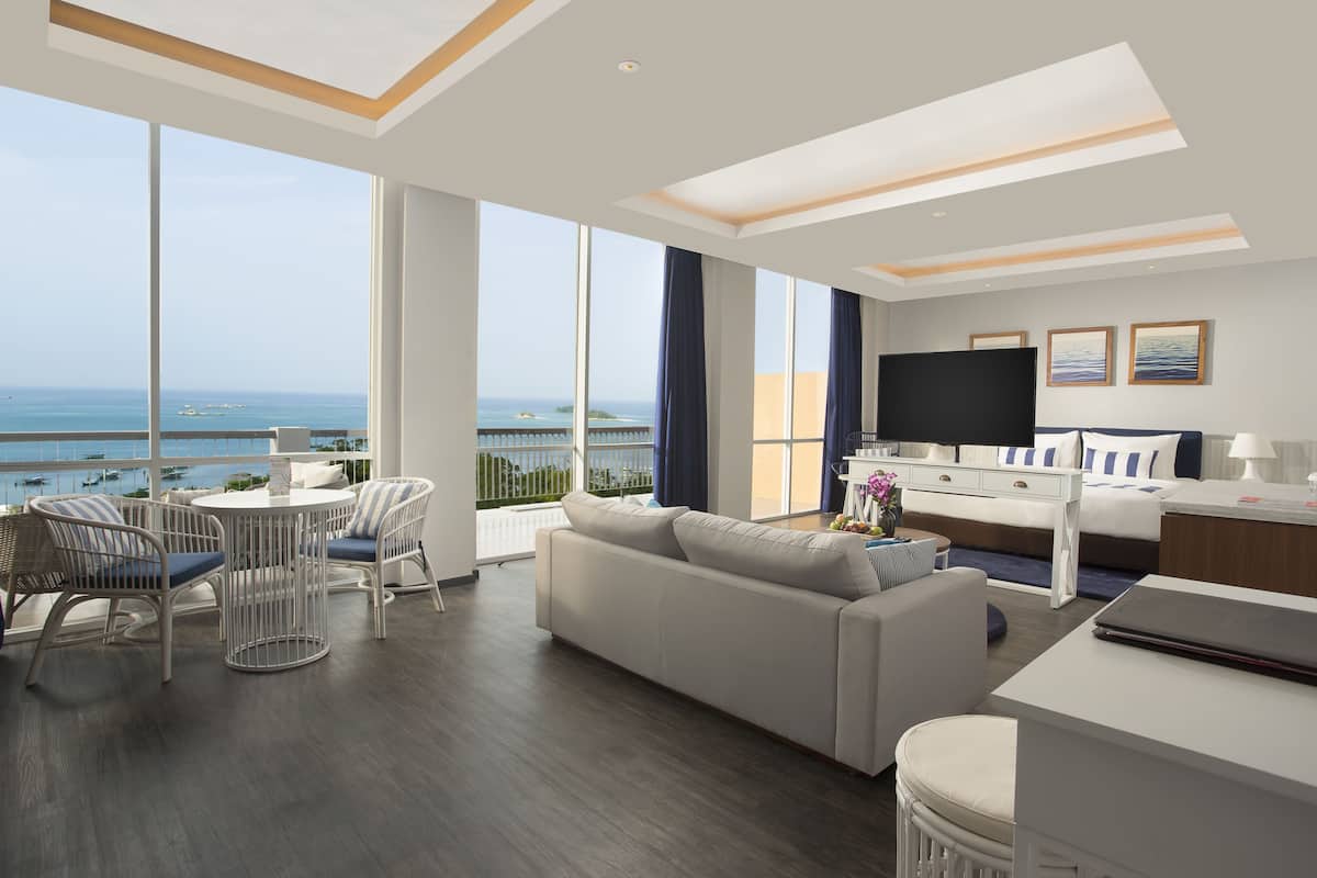 Une chambre d’hôtel moderne dotée d’un grand balcon, d’un canapé, d’une table à manger et d’un téléviseur.