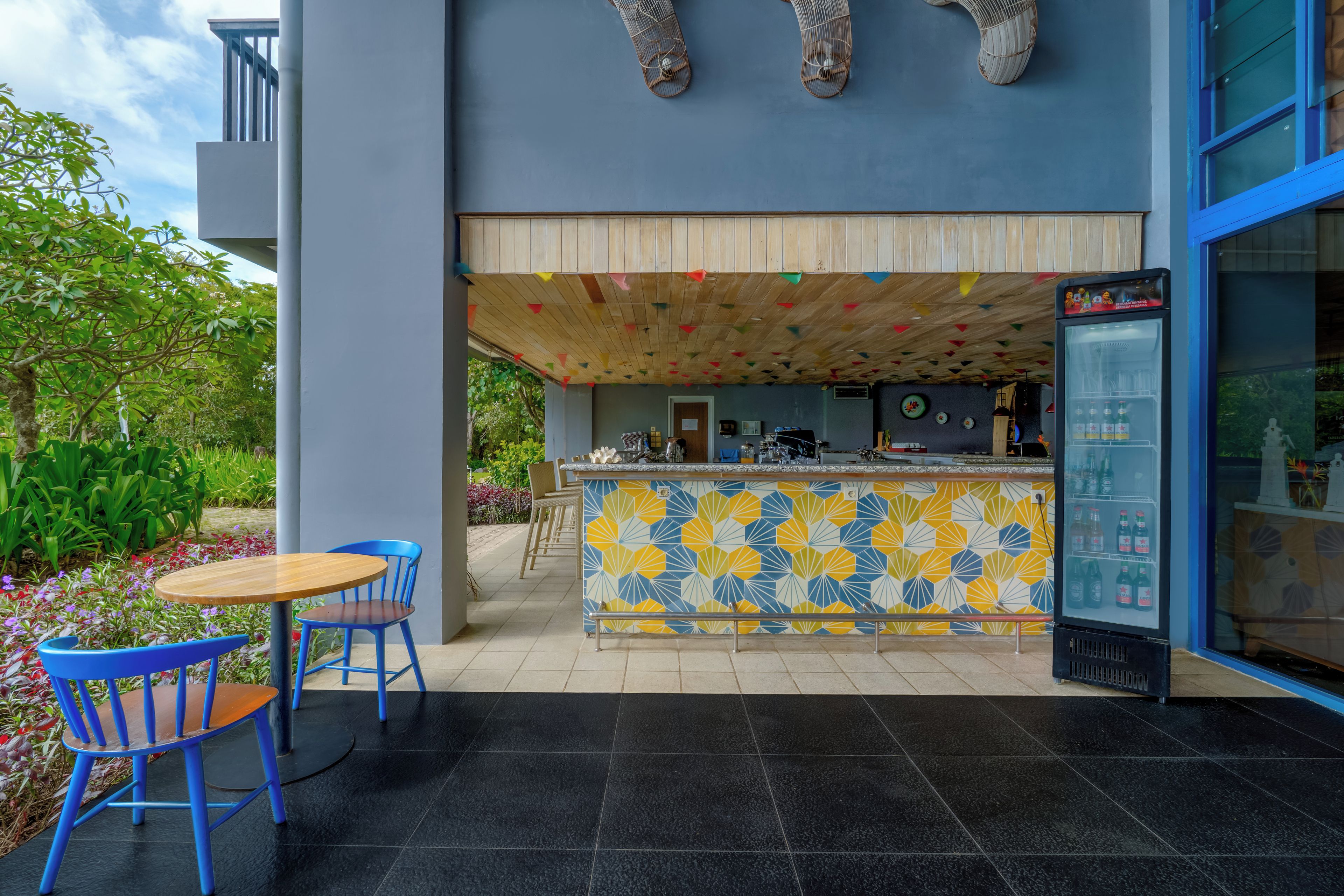 An outdoor bar area with a patterned tile backsplash, a refrigerator, and blue chairs.