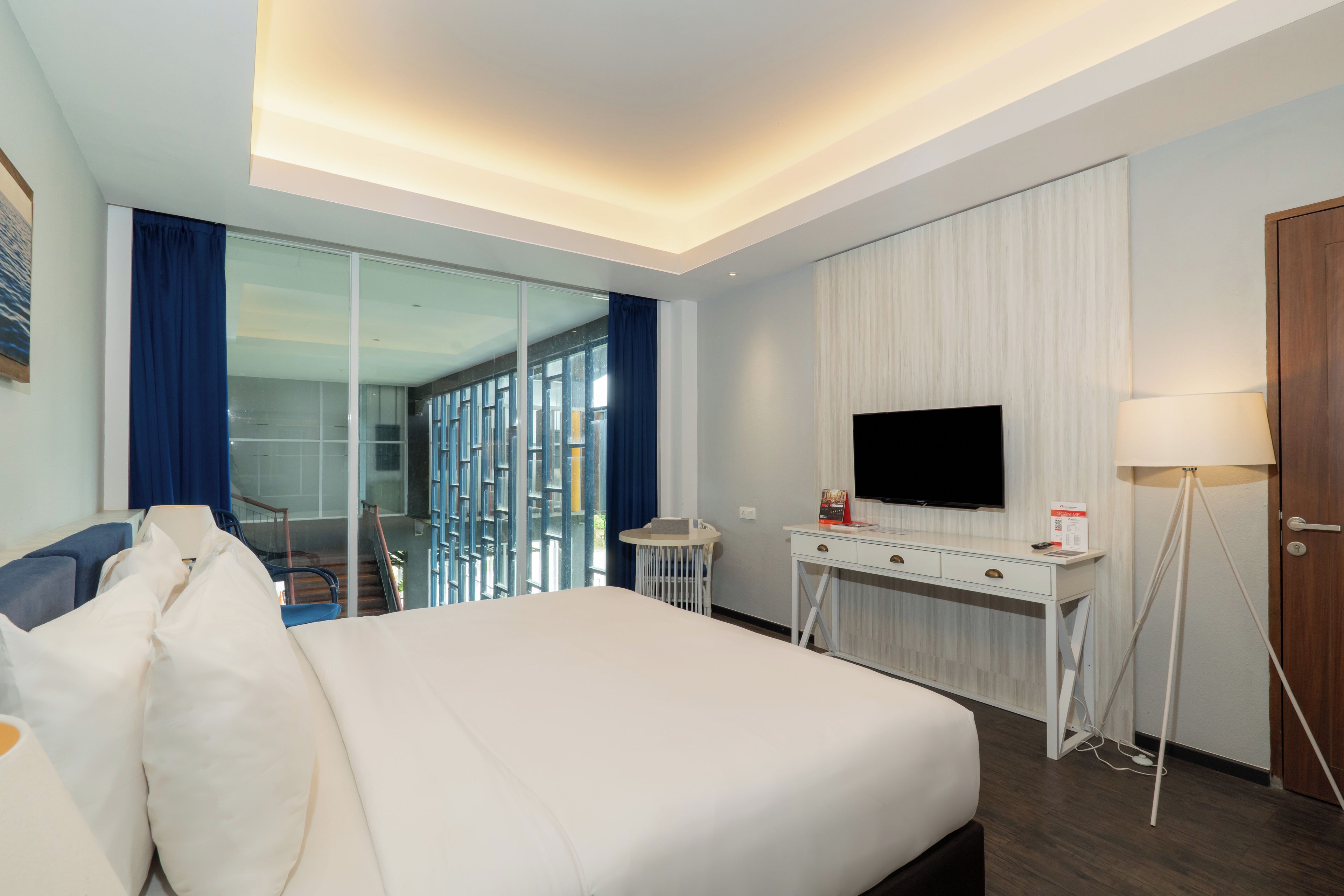 A hotel room with a bed, a desk, a TV, and a glass partition.