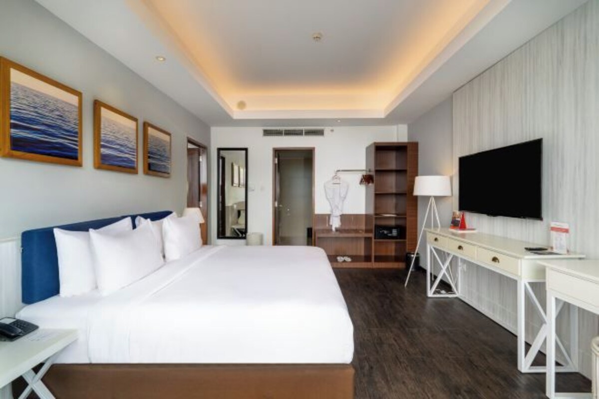 Une chambre d’hôtel avec un grand lit, un bureau doté d’un téléviseur à écran plat, une armoire et un miroir.