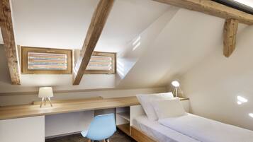 A bedroom with a sloped ceiling, wooden beams, a desk, a chair, a bed, and two bedside tables with lamps.