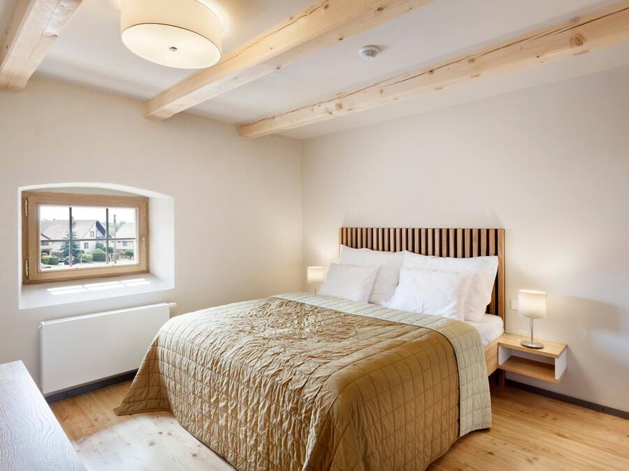 A bedroom with a wooden headboard, a window with a view, a bedside table with a lamp, and a bed with a quilted bedspread.